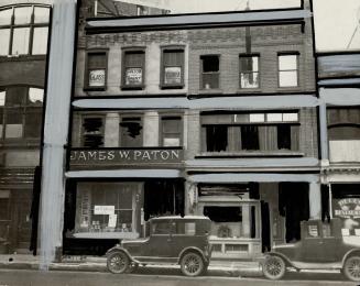 Exterior view of three-storey brick building. Sign above shop window reads, James W. Paton.