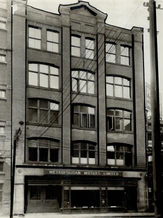 Façade of five-storey brick building. Sign above first floor windows reads, Metropolitan Motors ...