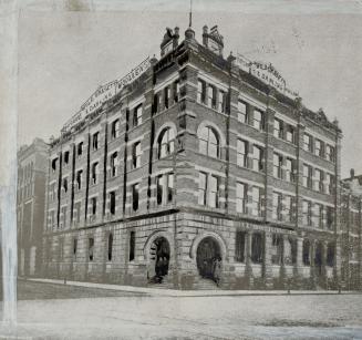 Corner view of four-storey brick building with arched stairwells left and right at corner of bu…