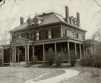 Three-storey brick structure with gables, several brick chimneys and wrap-around porch.