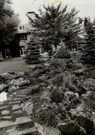 In foreground a flagstone path flanked by rock garden beds curves right, disappearing. Beyond,  ...
