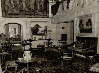 Paneled room full of dark wood seating, side tables, landscape paintings and hung tapestry.