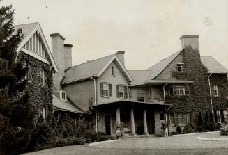 Exterior of three-storey, brick house with dark shutters and prominent chimney stacks; vines co ...