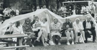 Soggy but smiling, some of the estimated 25,000 people who attended the International Picnic on Centre Island yesterday got some shelter from the rain(...)