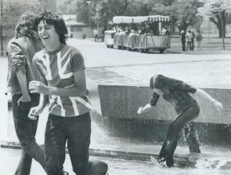 A girl steps out of a fountain after being dunked as two friends turn away laughing. 