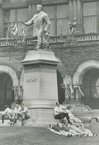 Siesta in the summer sun. Noon-hour idlers take their ease beneath the Queen's Park statue of Sir James Pliny Whitney while yesterday's warm sunshine (...)