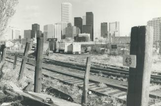Image shows railway tracks and vacant land behind them as well as high-rise Harbour buildings i ...