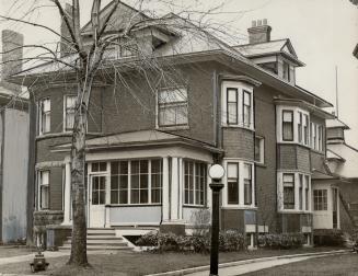 Exterior of three-storey brick house showing front with glassed-in porch and dormer window; rig…