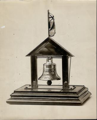 Bell suspended from slope-roofed structure mounted on beveled, rectangular base. Union Jack fla ...