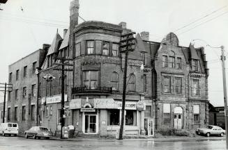 Corner view of three-storey brick building with narrow dormers. Sign above ground floor shop wi…