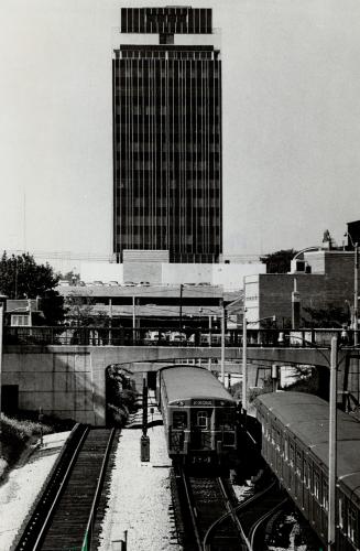 Image shows a few trains on tracks with a high-rise building in the background.