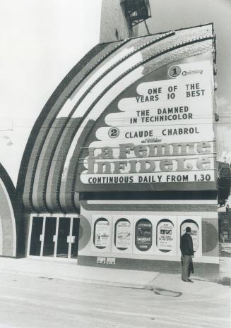Man stands in front of five movie advertisements beside cinema entrance. Billboard above reads, ...