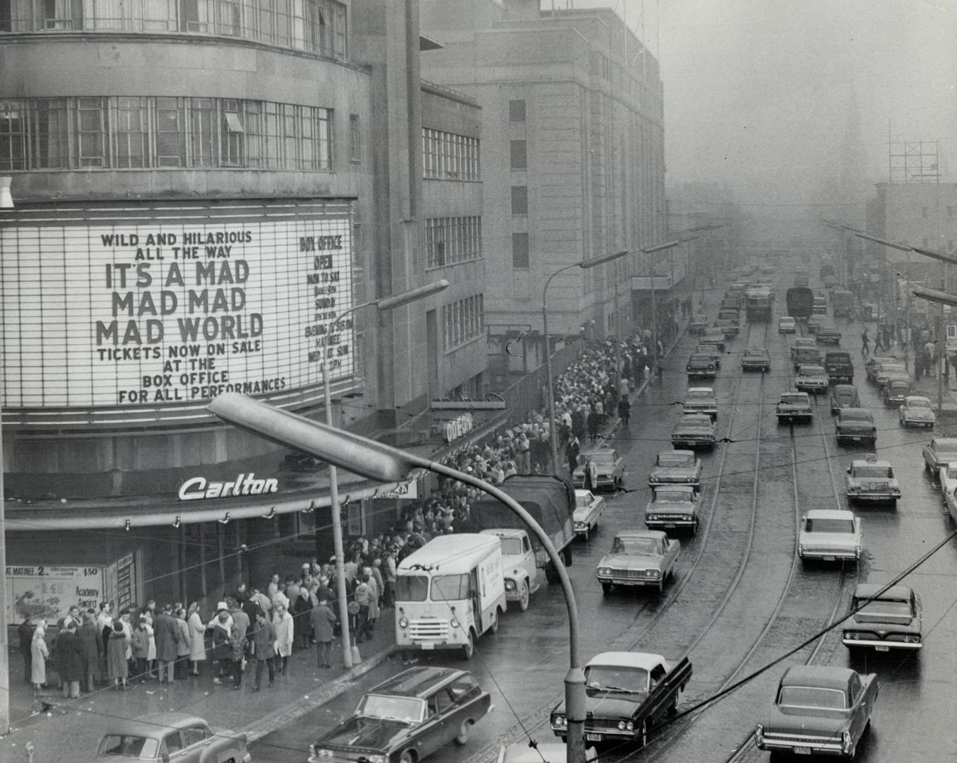 Overhead street view of people lined up around block outside cinema. Sign above entrance reads, ...