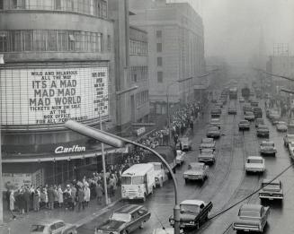 Overhead street view of people lined up around block outside cinema. Sign above entrance reads, ...