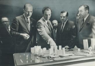 Image shows a group of people standing in front of the waterfront buildings' model on the desk.