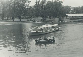 Image shows a cruise boat on the lake with a lot of trees on the shore in the background.