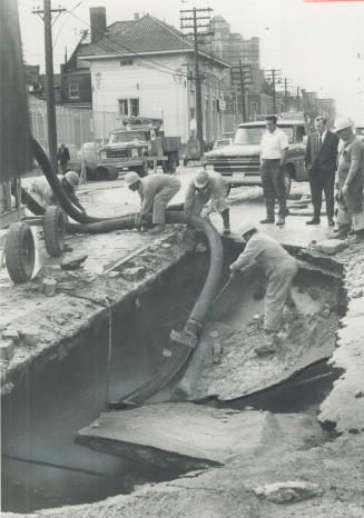 Image shows a crater in the street and some workers around it.