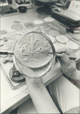 Painstaking detail of a medal Mrs. Dora de Pedery Hunt is making for the Metropolitan Toronto Zoo involves working with a scalpel and examining the work through a magnifying glass. The medal depicts an ark load of animals.