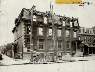 Three-storey brick structure with Mansard roof and dormer windows. Sign attached to leftmost gr ...