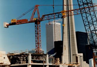 Image shows a few cranes at the construction site with a CN Tower in the background.