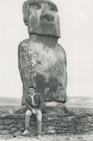 Archeologist sits, in front of giant island statue