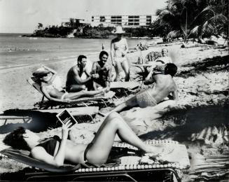 Leaving cares behind, a relaxed group of vacationers at Guadeloupe's Club Med takes it easy on a sunny stretch of beach