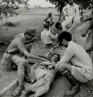 Relaxing in a bamboo stretcher, this Chinese soldier gets his arm wound treated at an emergency dressing station set up on a road near the battlefield