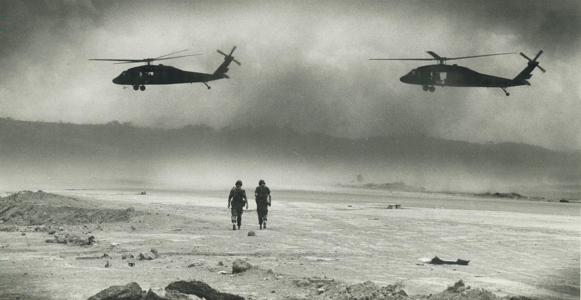 Grenada scene: Helicopters approach a landing strip while soldiers walk along beach