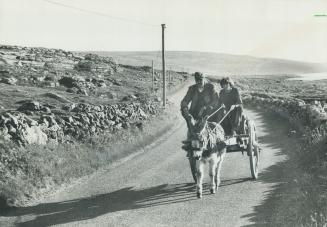 They day's work done, a young Irish lad and his father head home by donkey cart along the winding coastal road of County Clare which borders the waters of Galway Bay