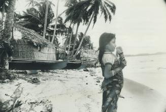 A young girl holds her crude wooden dool and gazes out over the Caribbean