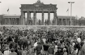 Historic symbol: Throngs of West Germans gaze up at East German border quards atop the Berlin Wall, in front of the Brandenburg Gate