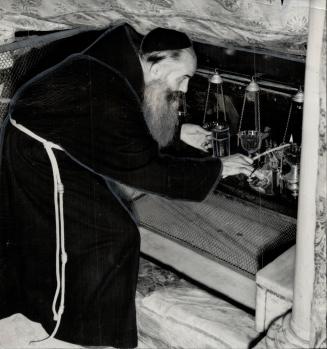 Unheeding menace of war which may shatter the peace of Bethlehem, Brother Camillus lights the lamps in the manger in the Church of the Nativity where the Child Jesus was laid after birth