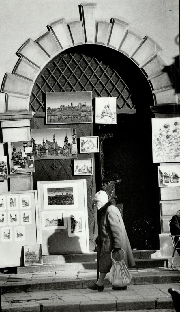 Old woman walks past artist's display in an ornately designed doorway