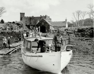 Two men on a boat pulling away from a dock. A turreted castle appears in the background, and ma ...
