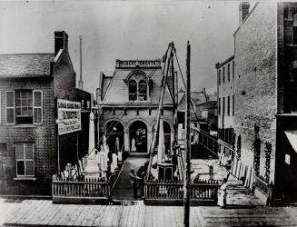 In 1871 number 80 on King St. W., the present site, was occupied by the Canadian Hydraullic Marble Works, Robert Forsyth, owner. Note the wooden sidewalk and picket fence