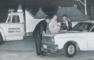 Bomb Disposal Police and detective gingerly examine five sticks of dynamite found sitting on the hood of a car in the parking lot of Eastern High Scho(...)