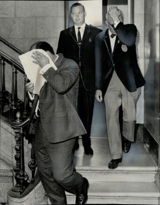 Charged with conspiracy, Michael Meyer Rush (left) and Joseph Williams attempt to shield their faces from photographers as a detective escorts them downstairs at police headquarters