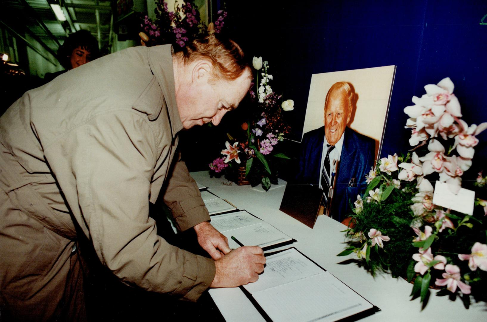 A portrait of Harold Ballard smiles up at Red Kelly, former Leafs hockey player and coach, as he signs a guest book yesterday at the Gardens. About 4,(...)