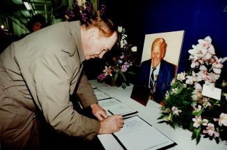 A portrait of Harold Ballard smiles up at Red Kelly, former Leafs hockey player and coach, as he signs a guest book yesterday at the Gardens. About 4,(...)
