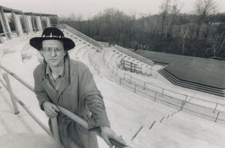 A man stands a the top of the range of seats in front of an outdoor amphitheater.