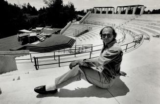 A man poses casually at the top of an outdoor amphitheater.