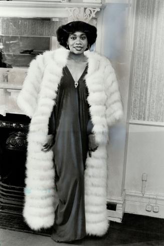 Nightclub-TV singer Donna Best wears gray silk evening dress by Wayne Clark, maribou coat by Claire Haddad