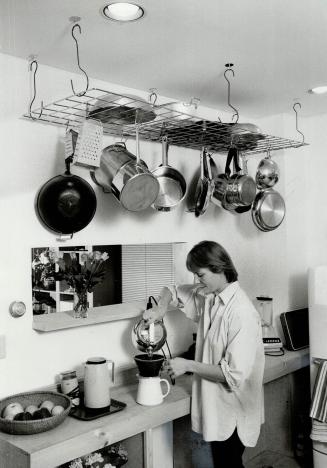 Space saver: pots and pans hang from ceiling grid in stark white kitchen where Cadeau makes coffee