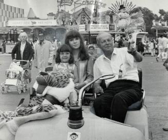 King of the midway, Patty Conklin takes two young guests, Karen Wilson,6, and Donna Wilson, 16, on a tour of Exhibition grounds in his green golf cart
