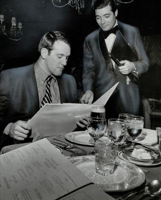 Charge it to Mr. Cahill. Jim Corrigall looks over menu at Fifty-Fourth dining room. He was guest of Argo coach Leo Cahill for dinner of wine and lobster