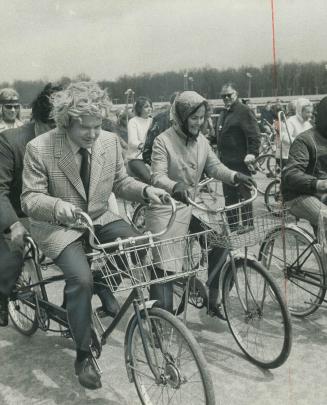Ontario Premier William Davis, wearing woman's blonde wig, takes over the driver's seat of a bicycle built-for-two while Windsor Mayor Frank Wansbroug(...)