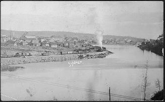 Black and white photograph of a medium sized town built beside a lake.