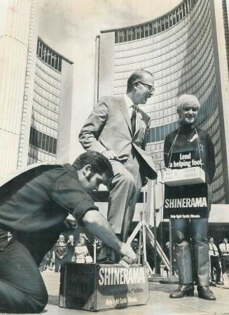 Polishing up to the Mayor. Mayor William Dennison gets a shoe shine from Ryerson Polytechnical student Bob Robinson while Gloria Demkowich looks on wi(...)