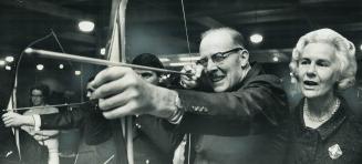 The Archer. Mayor William Dennison, with wife encouraging him, draws bead on target at Sportsmen's Show as host to Ontario mayors and reeves last nigh(...)