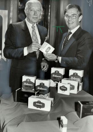 Profit-maker: J. H. Devlin, chairman of Rothmans of Pall Mall Canada Ltd., Left, accepts cigarette from company president Robert Hawkes at company annual meeting